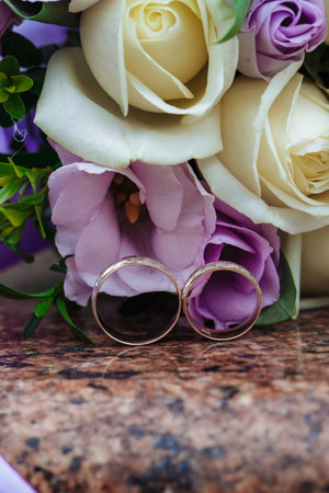 Wedding rings on granite stand against the background of a beautiful bouquet of flowersの写真素材