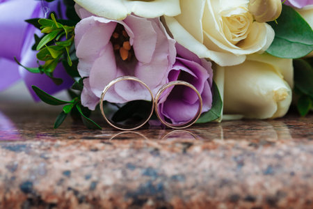 Wedding rings on granite stand against the background of a beautiful bouquet of flowersの写真素材