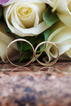 Wedding rings on granite stand against the background of a beautiful bouquet of flowersの写真素材