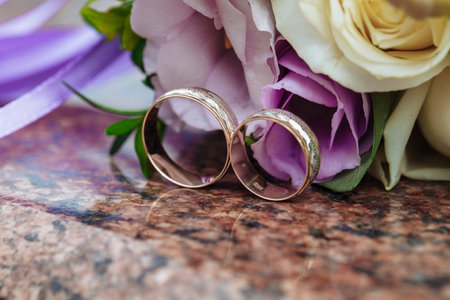 Wedding rings on granite stand against the background of a beautiful bouquet of flowersの写真素材