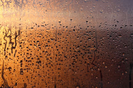 Frozen drops of condensation on a transparent glass window in the winter season with natural sunlight through the glass, high humidity, temperature difference, natural backgroundの写真素材
