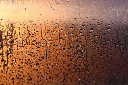 Frozen drops of condensation on a transparent glass window in the winter season with natural sunlight through the glass, high humidity, temperature difference, natural backgroundの写真素材