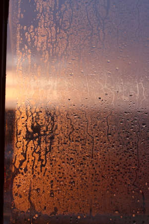 Frozen drops of condensation on a transparent glass window in the winter season with natural sunlight through the glass, high humidity, temperature difference, natural backgroundの写真素材