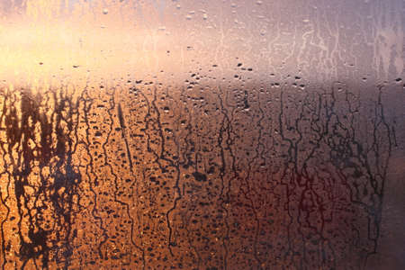 Natural background of condensation of water on a window glass with high air humidity, large drops dripping. Natural sunlight through glass. High humidityの写真素材