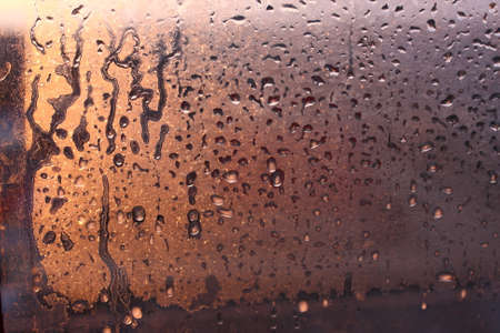 Natural background of condensation of water on a window glass with high air humidity, large drops dripping. Natural sunlight through glass. High humidityの写真素材