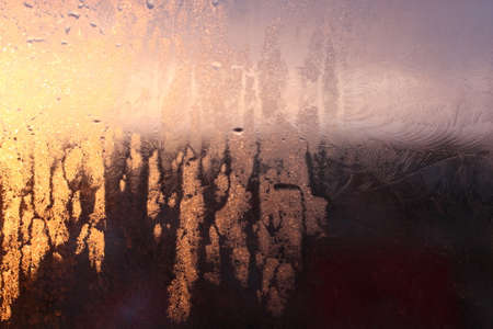 Frozen drops of condensation on a transparent glass window in the winter season with natural sunlight through the glass, high humidity, temperature difference, natural backgroundの写真素材