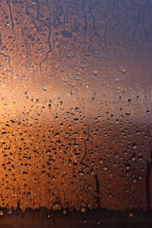 Window transparent glass with condensation, high humidity in the room, large drops of water flow down, warm tone, natural dropsの写真素材