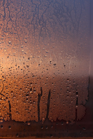 Window transparent glass with condensation, high humidity in the room, large drops of water flow down, warm tone, natural dropsの写真素材