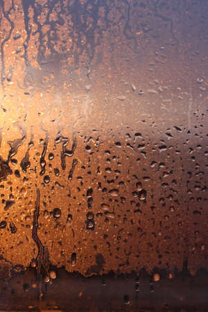 Natural background of condensation of water on a window glass with high air humidity, large drops dripping. Natural sunlight through glass. High humidityの写真素材
