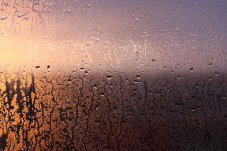 Window transparent glass with condensation, high humidity in the room, large drops of water flow down, warm tone, natural dropsの写真素材
