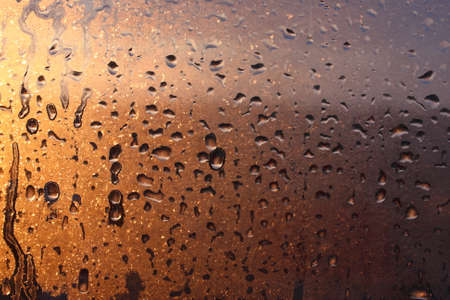 Window transparent glass with condensation, high humidity in the room, large drops of water flow down, warm tone, natural dropsの写真素材