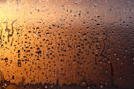 Window transparent glass with condensation, high humidity in the room, large drops of water flow down, warm tone, natural dropsの写真素材