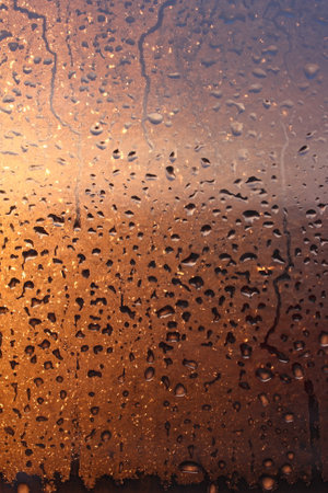 Natural background of condensation of water on a window glass with high air humidity, large drops dripping. Natural sunlight through glass. High humidityの写真素材