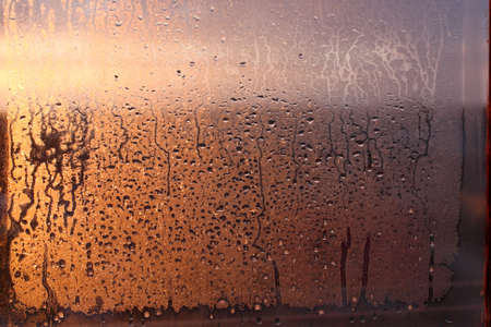 Window transparent glass with condensation, high humidity in the room, large drops of water flow down, warm tone, natural dropsの写真素材