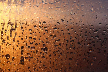 Window transparent glass with condensation, high humidity in the room, large drops of water flow down, warm tone, natural dropsの写真素材