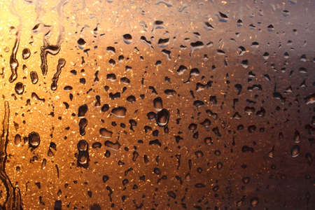 Window transparent glass with condensation, high humidity in the room, large drops of water flow down, warm tone, natural dropsの写真素材
