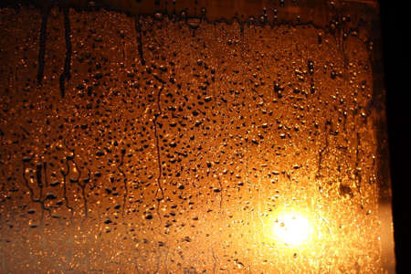 Natural background of condensation of water on a window glass with high air humidity, large drops dripping. Natural sunlight through glass. High humidityの写真素材