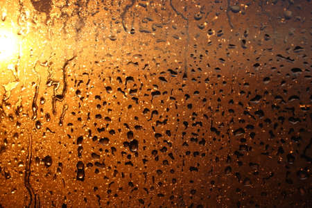 Window transparent glass with condensation, high humidity in the room, large drops of water flow down, warm tone, natural dropsの写真素材