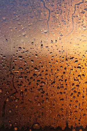 Vertical natural background with water drops on a window with sun rays, condensation on glass with dripping dropsの写真素材