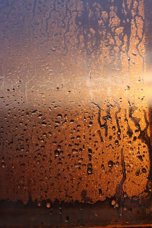Vertical natural background with water drops on a window with sun rays, condensation on glass with dripping dropsの写真素材