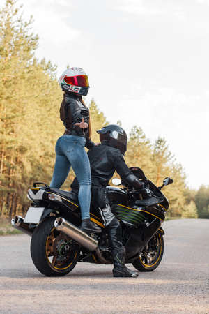 Motorcyclist in protective equipment and helmet shows fuck with a middle finger while sitting with a girl on a motorcycleの写真素材