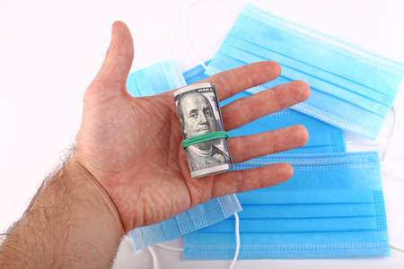 One hundred dollars in hand against the background of a medical mask from coronavirus