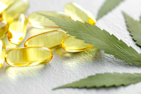CBD oil pills. Group of transparent CBD cannabidiol capsules and hemp leaves on white background. Organic dietary supplements conceptの写真素材