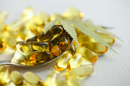 CBD oil pills. Group of transparent CBD cannabidiol capsules and hemp leaves on white background. Organic dietary supplements conceptの写真素材