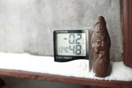 Chocolate Santa Claus and measuring temperature and humidity, thermometer and a hygrometer on window with snow against background of frozen glassの写真素材