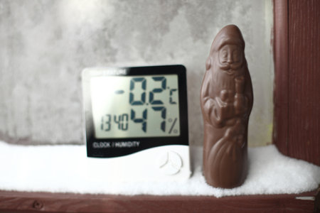 Chocolate Santa Claus and measuring temperature and humidity, thermometer and a hygrometer on window with snow against background of frozen glassの写真素材