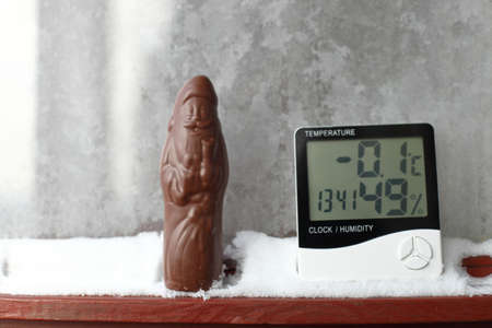 Chocolate Santa Claus and measuring temperature and humidity, thermometer and a hygrometer on window with snow against background of frozen glassの写真素材