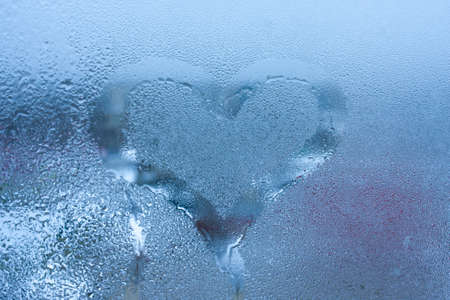 Closeup on love heart condensation inscription over sweaty window glass background. Valentine creative symbol concept. Hand draw heart on misty windowの写真素材