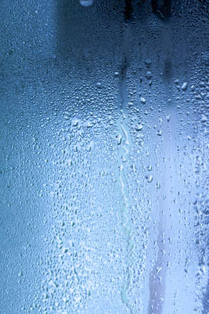 Blue background of natural water condensation, window glass with high air strong humidity, large drops drip. Collecting and streaming downの写真素材