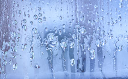 Blue background of natural water condensation, window glass with high air strong humidity, large drops drip. Collecting and streaming downの写真素材