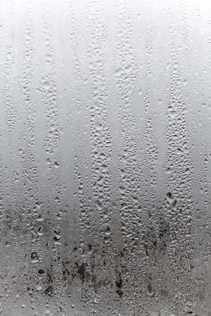 Vertical natural background, condensation on glass with drops flowing down, humidity and foggy blank. outside, bad weather, rainの写真素材