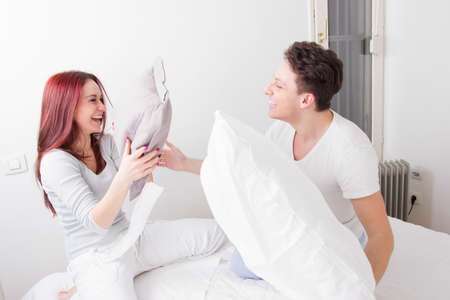 young smiling man and woman fighting with pillows together in bed as sign of happy relationshipの写真素材