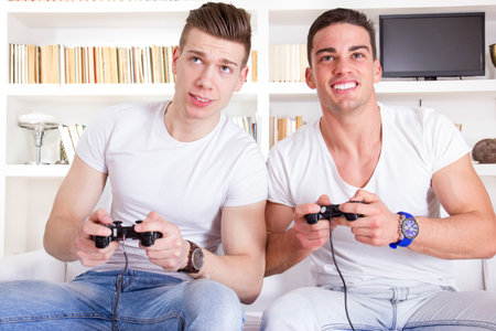 two male friends playing video game with controllers at home