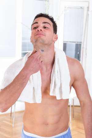 handsome man shaving beard with razor in hand ad towel around neckの写真素材