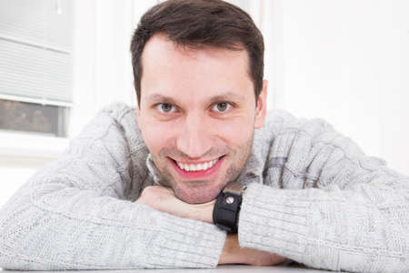 Closeup portrait of a young attractive man with great toothy smile leaning on the table at home indoorsの写真素材