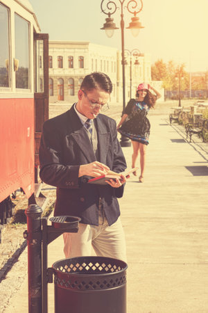 Beautiful vintage style couple outside retro train coach have a romantic encounter while he reading ...