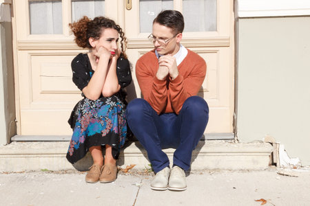 depressed and agitated man and woman crouching in front of the house at stairwell because problem...