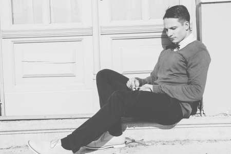 young man in sweater sitting on steps in front of house and posing , black and white photoの写真素材