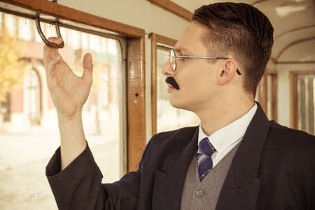 man with a mustache in a suit with glasses posing in an old train wagon or carriage and trying to open window with hand , retro vintage fashion photoの写真素材