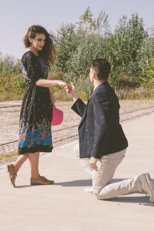 retro vintage young man kneeling and asking a girl to marry him in the park on the sidewalk next to the bench , walk with affectionの写真素材