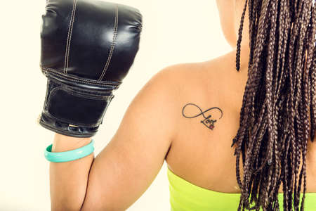 Photo of young woman from behind showing black boxing glove with love tattoo on her back の写真素材