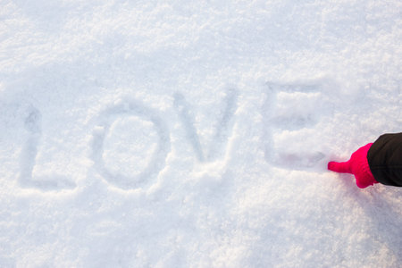 written or drawn by hand in pink glove word LOVE on white snow, romantic image composition. Human hand write or drawing letters on snow in winter timeの写真素材