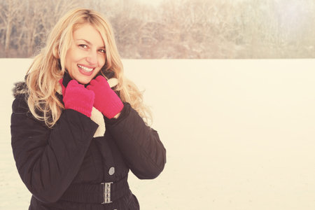 winter happy woman in snow looking up at camera, copy space outside on sunny cold winter vintage day. Portrait Caucasian smiling female model with pink gloves holding white scarf in first snowの写真素材