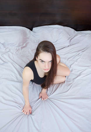 Portrait of sexy young  passionate woman or girl lying on gray sheet bed at bedroom in seductive pose and looking to camera or you.の写真素材