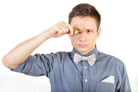 Young serious man in shirt and bow tie holds door locker. Male person holding key over white background.の写真素材