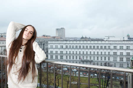 Beautiful carefree girl standing on balcony with city in the background , Young thoughtful woman with long hair enjoying misty morningの写真素材